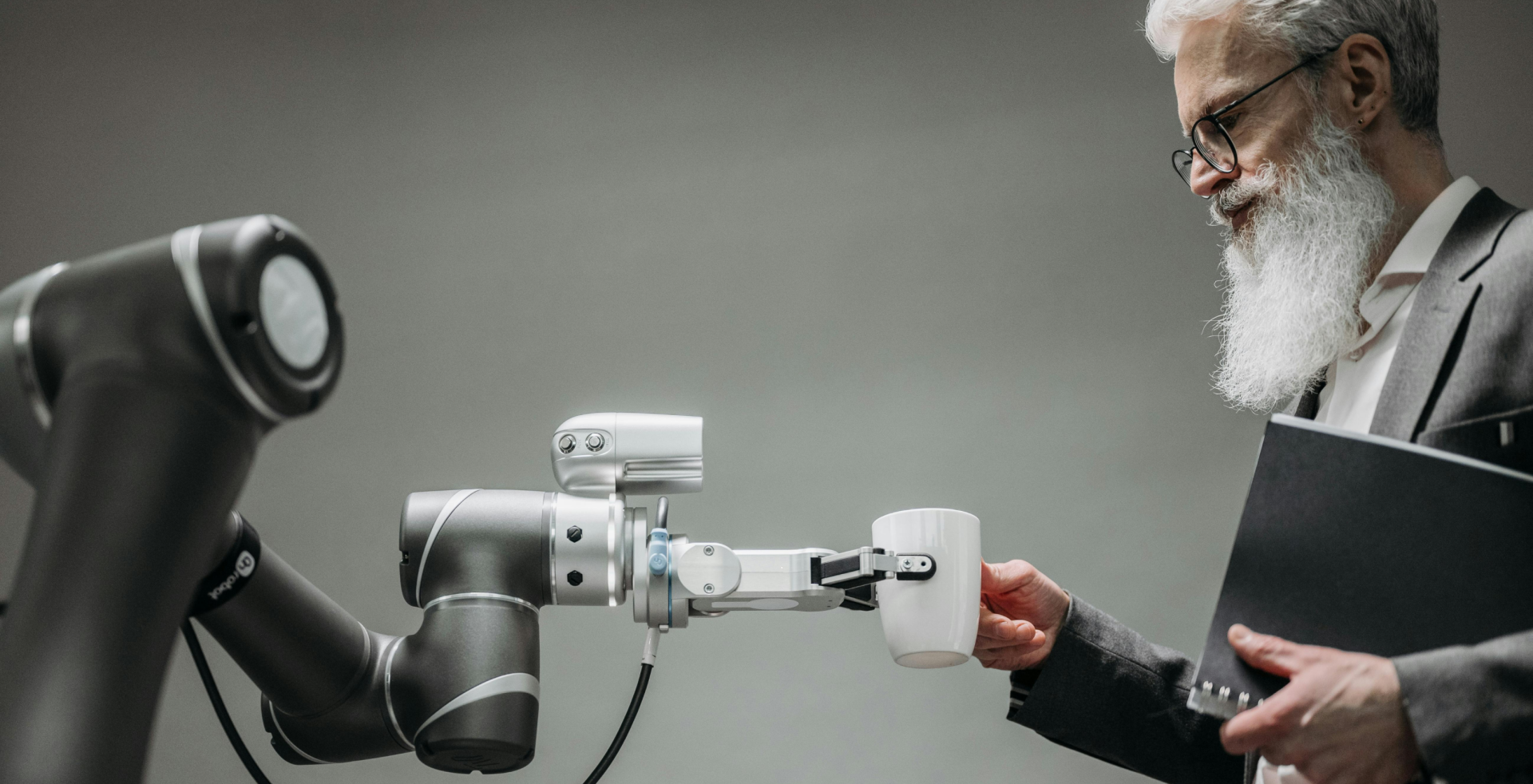 Robot barista serves a cup of coffee to a person with a large white beard