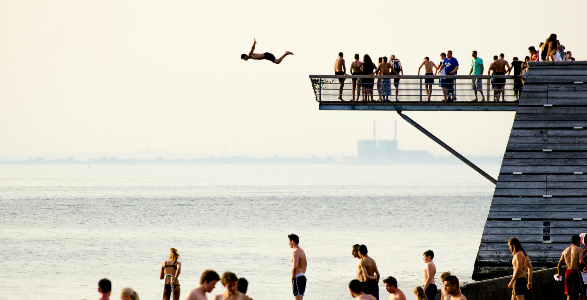 Person dives from a high diving board in front of a large group of people