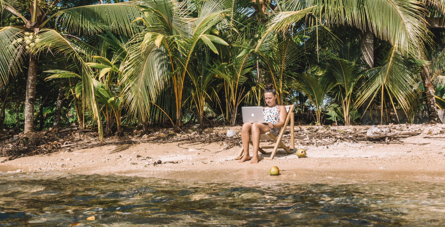 Woman lounges on a beach with a laptop open in her lap