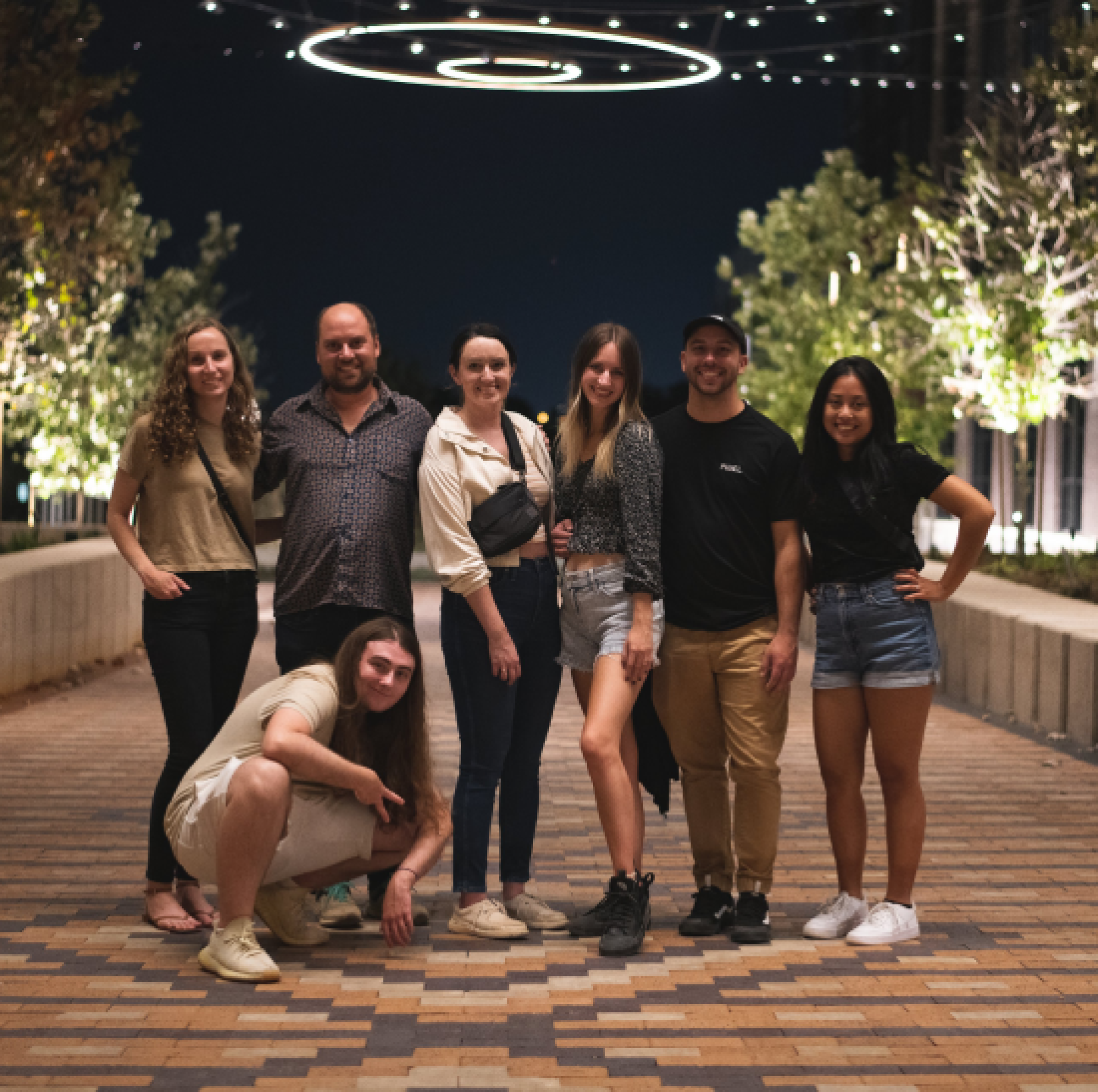 A group of By the Pixel team members posing for a photo at night on a well-lit, decorative brick walkway